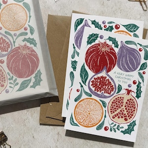May include: Greeting cards with fruit illustrations, including pomegranates, figs, and oranges, in shades of red, purple, and orange. The cards are decorated with green holly leaves and berries. One card reads "A Very Happy Christmas to You."