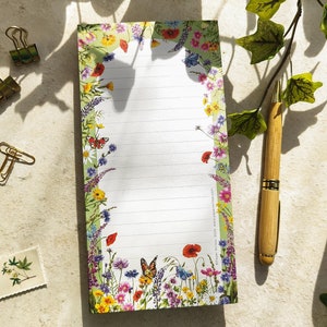 May include: A notepad with a floral design featuring butterflies, poppies, and other wildflowers. The notepad has a green background and white lined paper.