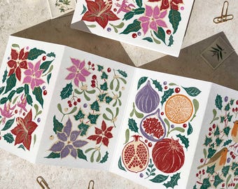 May include: Greeting cards with floral and fruit designs. The cards feature illustrations of poinsettias, figs, pomegranates, and oranges in red, pink, purple, and green. The cards are folded and displayed on a light-colored surface.