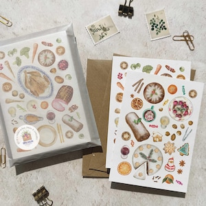 May include: A set of blank cards and envelopes featuring watercolor illustrations of a holiday feast. The cards depict a roasted turkey, ham, and various side dishes. The design includes a Christmas cake, oranges, and festive decorations. The cards are packaged in a clear cellophane sleeve.