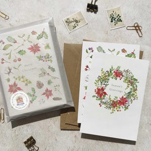 May include: Christmas greeting cards with floral designs. One card reads "Merry Christmas" and another says "Season's Greetings." The cards feature illustrations of poinsettias, holly, and other seasonal foliage. The cards are packaged with brown envelopes.