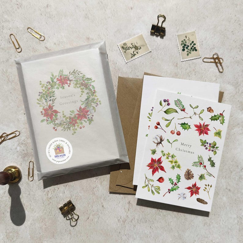 May include: Christmas greeting cards with floral designs, including poinsettias, holly, and berries. One card reads "Season's Greetings" in a wreath, and another says "Merry Christmas". The cards are accompanied by envelopes, paper clips, and stamps.