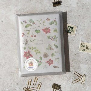 May include: A set of folded blank Christmas cards and envelopes, packaged in a clear cellophane sleeve. The card design features watercolor illustrations of festive botanical elements and the words "Merry Christmas". Gold paper clips and stamps are scattered around the package.