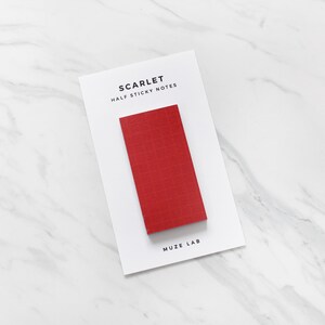 Könnte beinhalten: Eine weiße Karte mit dem Text "SCARLET HALF STICKY NOTES" und einem rechteckigen roten Haftnotizblock. Die Karte trägt auch den Text "MUZE LAB" am unteren Rand. Der Hintergrund ist eine weiße Marmoroberfläche.