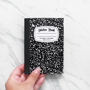 May include: A black and white composition notebook with a sticker book label. The label says "Sticker Book" and includes the details "16 sheets / 32 pages 5.5 x 5 in".