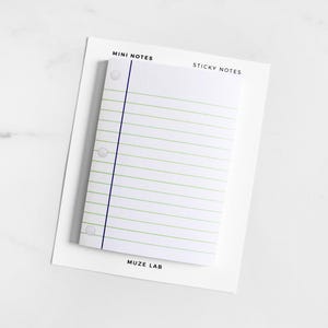 May include: A rectangular pad of white sticky notes featuring a lined design with a vertical dark blue margin line and three circular hole punch graphics on the left side. The backing card displays the text MINI NOTES, STICKY NOTES, and MUZE LAB.
