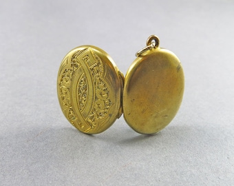 May include: A gold locket with an engraved floral design on one side and a plain surface on the other side.