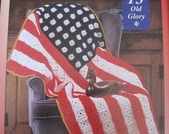May include: A crocheted American flag blanket draped over a chair with a wooden duck figurine on top. The blanket is red, white, and blue with a yellow border. The chair is gray and has wooden legs. The text "13 Old Glory" is visible in the upper right corner of the image.
