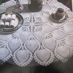 May include: White crocheted doily tablecloth with a floral design. A black and white floral teapot and a cup of coffee are on the table.