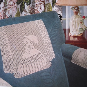 May include: A teal blue armchair with crocheted doilies on the seat and armrest. The doilies feature a delicate floral design. The armchair is in front of a floral patterned wallpaper.