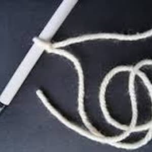 May include: A white knitting needle with a white yarn loop on the end. The yarn is wrapped around the needle and a ball of white yarn is in the background.