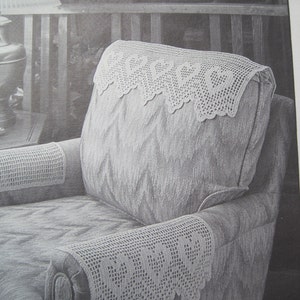May include: A grayscale image of a chair with crocheted arm and headrest covers. The covers are a light color and feature a decorative, openwork design along the edges. The chair has a patterned fabric.