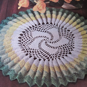 May include: A crocheted doily with a spiral design in the center. The doily is made in shades of green, yellow, and white.