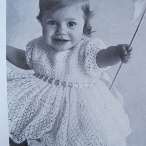May include: A young girl wearing a white crocheted dress with a beaded belt. The dress has a lacy pattern and is worn with a white headband. The girl is holding a white and blue pinwheel.