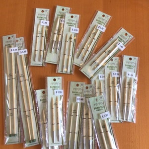 Peut inclure: Plusieurs aiguilles à tricoter en bambou dans des emballages transparents. Les aiguilles sont de différentes tailles et portent la marque "Knitter's Pride Bamboo Charm". Des étiquettes de prix sont visibles. Sur une surface brune.