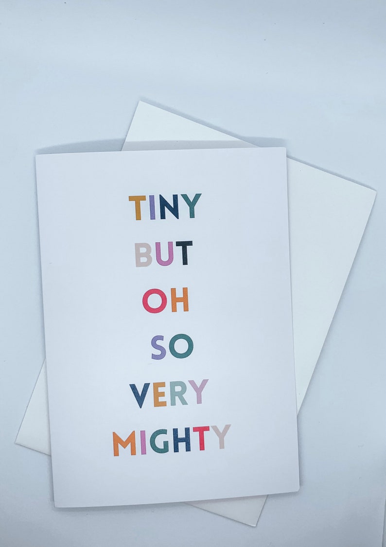 May include: A white greeting card featuring the phrase "TINY BUT OH SO VERY MIGHTY" in colourful block letters. The card is accompanied by a white envelope, ideal for sending messages.