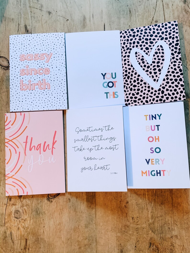 May include: A selection of greeting cards with different designs and text. One card says "sassy since birth" on a polka dot background. Another says "You Got This." Other cards say "thank you," and "Tiny but oh so very mighty."