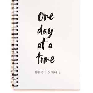 May include: White spiral bound notebook with the text "One day at a time" written in black cursive. The bottom of the notebook says "NICU Notes & Thoughts".