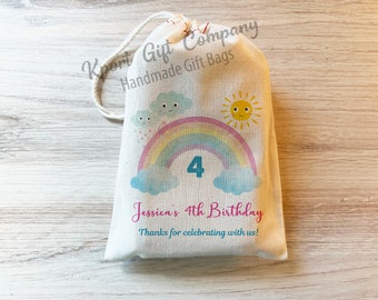 May include: A white cotton gift bag with a rainbow, clouds, and a sun design. The bag has the text "Jessica's 4th Birthday" and "Thanks for celebrating with us!" printed on it.