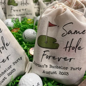 May include: Off-white drawstring fabric pouch featuring a printed graphic of a green golf putting hole with a red flag. The text reads Same Hole Forever, Jordan's Bachelor Party, and August 2023 in black script and block lettering.