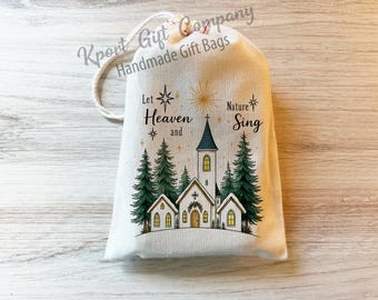 May include: A cream-colored fabric drawstring gift bag featuring a printed illustration of a church surrounded by evergreen trees. The text reads Let Heaven and Nature Sing. The design includes gold stars and a sunburst above the church steeple.