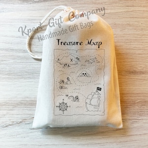 May include: A white cotton drawstring bag with a black and white treasure map design. The map features a skull and crossbones, a pirate ship, and the words "Treasure Map".