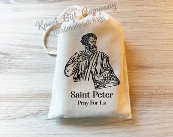 May include: A cream-colored drawstring gift bag featuring a black line-art illustration of Saint Peter holding keys. Below the image, the text reads Saint Peter and Pray For Us in a black serif font. The bag has a white cord drawstring closure.