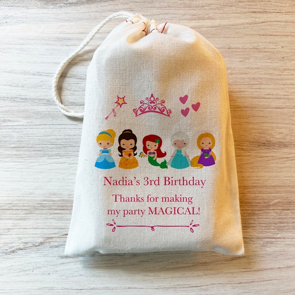 May include: A cream-colored drawstring fabric pouch featuring a printed graphic of five cartoon princesses, a pink wand, a tiara, and three hearts. The text reads: Nadia's 3rd Birthday. Thanks for making my party MAGICAL! with a decorative line below.