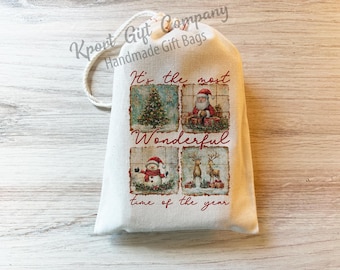 May include: A cream-colored fabric drawstring gift bag featuring a printed design with four square panels showing a Christmas tree, Santa Claus, a snowman, and reindeer. The text reads, It's the most wonderful time of the year in red script.