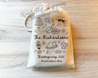 May include: Off-white canvas gift bag with a drawstring closure. The bag is decorated with Thanksgiving-themed illustrations, including a turkey, football, and wine glasses. Text on the bag reads "The Richardsons" and "Thanksgiving 2025 Kennebunkport, Maine."