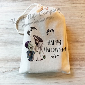 May include: A white cotton drawstring bag with a printed design of a cartoon couple dressed as Frankenstein's monster and his bride. The bag has the text "Happy Halloween!" printed on it.