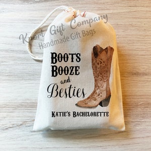 May include: A white drawstring gift bag with the text "Boots, Booze, and Besties" and a watercolor illustration of a brown cowboy boot. The text "Katie's Bachelorette" is also printed on the bag.