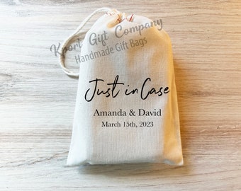 May include: A cream-colored fabric drawstring gift bag featuring the black printed text Just in Case, Amanda & David, and March 15th, 2023. The bag includes a white cord closure at the top and a watermark reading Koort Gift Company Handmade Gift Bags.