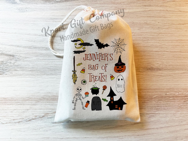 May include: A cream-colored Halloween-themed gift bag with a drawstring closure. The bag is decorated with various Halloween illustrations, including a bat, spiderweb, pumpkin, ghost, and skeleton. The text "Jennifer's Bag of Treats!" is printed on the front.