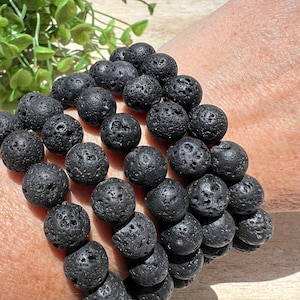 Op de afbeelding: Een set van vier zwarte lavastenen kralen armbanden. De armbanden zijn gestapeld op de pols van een persoon.