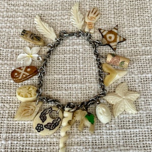 May include: A silver chain bracelet with multiple charms, including a star, a hand, a leaf, a flower, and an elephant. The charms are made of white bone and have intricate carvings.