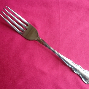 May include: A silver fork with an ornate handle on a pink background.