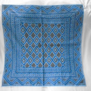 May include: A square scarf featuring a repeating diamond pattern in shades of blue and grey. The design includes a central grid of diamonds surrounded by multiple borders with geometric chevron and linear motifs in a consistent blue and grey color palette.