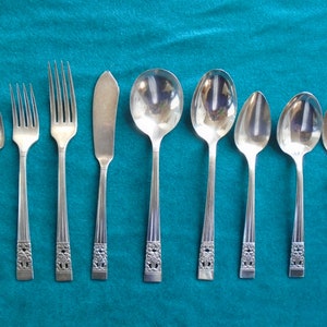 May include: A set of eight silver-plated utensils, including forks, spoons, and a butter knife. The utensils have an ornate design with a floral pattern.