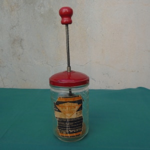 May include: A red and glass food mill with a metal crank. The label on the jar reads "Farmers Union Vegetable Mill".