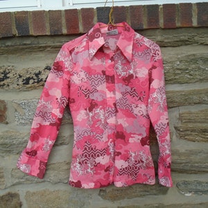 Op de afbeelding: Een roze overhemd met lange mouwen met een geometrisch patroon van wolken en swirls. Het overhemd heeft een knoopsluiting aan de voorkant en een kraag.