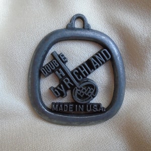 Puede incluir: Un llavero de metal de color plateado con las palabras "Double H by Richland" y "Made in U.S.A."  El llavero presenta un diseño estilizado de una herradura y un martillo cruzado.