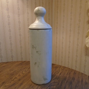 Może przedstawiać: Biały ceramiczny słoik z pokrywką i fakturowaną powierzchnią. Słoik ma okrągły wierzchołek i cylindryczny korpus.