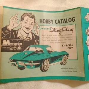 May include: An open brochure featuring a teal Corvette Sting Ray model car. The brochure is labeled "Hobby Catalog" and includes a drawing of a man giving an "okay" hand gesture. The brochure also shows other model cars.