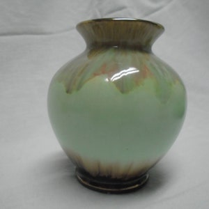 Könnte beinhalten: Eine kleine, grüne Keramikvase mit braunen und goldenen Akzenten. Die Vase hat einen runden Körper und eine ausgestellte Lippe.