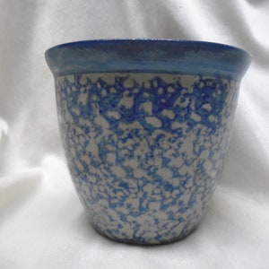May include: A blue and white ceramic planter with a speckled glaze. The planter has a rounded shape and a blue rim.
