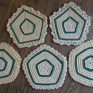 May include: Five crocheted hexagon-shaped placemats in beige and green. The placemats have a multi-layered design with a central hexagon surrounded by concentric rings of beige and green crochet.