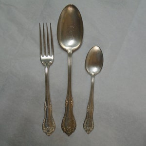 Peut inclure: Un ensemble de trois couverts en argent plaqué, comprenant une fourchette et deux cuillères. La fourchette a trois dents et un manche décoratif. La plus grande cuillère a un bol arrondi et un manche décoratif. La plus petite cuillère a un bol arrondi et un manche décoratif.