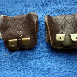 Puede incluir: Dos bolsas de cuero marr&oacute;n con cierres met&aacute;licos. Las bolsas tienen un dise&ntilde;o decorativo en la parte delantera.