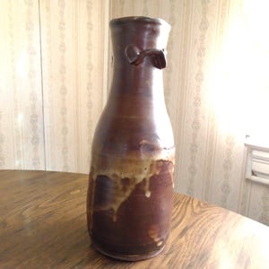 Botella de gres firmada y hecha a mano: Esmalte marrón antigoteo, asas aplicadas (borde desportillado)